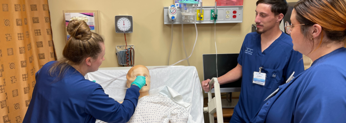 Three health science students in class treating mannequin 